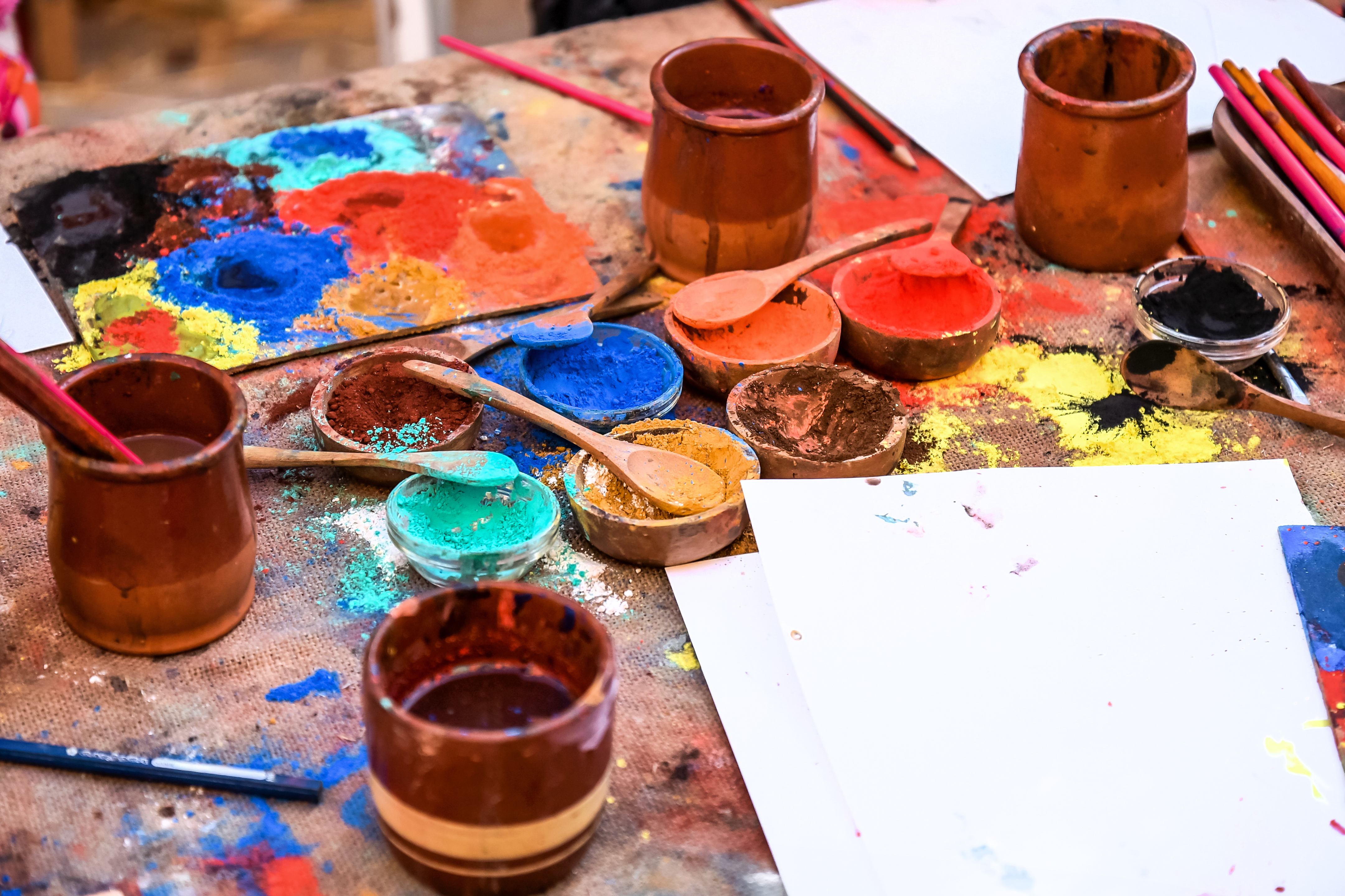 A wooden shelf containing compartments filled with vibrant powdered pigments in a variety of colors